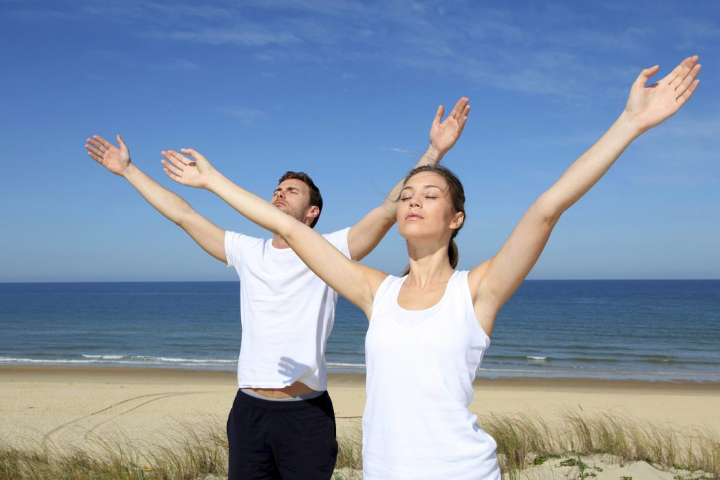 Couple meditating at the beach with arms up